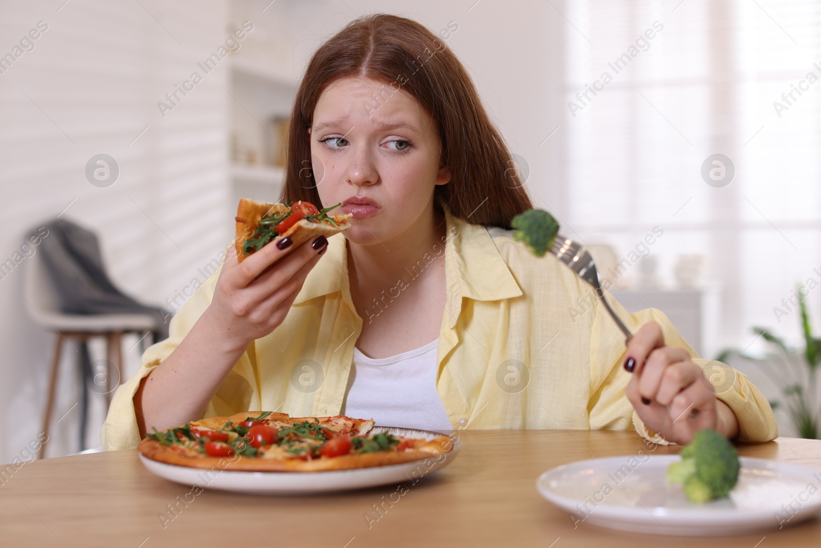 Photo of Sad teenage girl with piece of pizza at wooden table indoors. Eating disorder