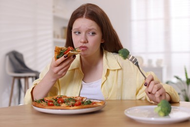 Photo of Sad teenage girl with piece of pizza at wooden table indoors. Eating disorder