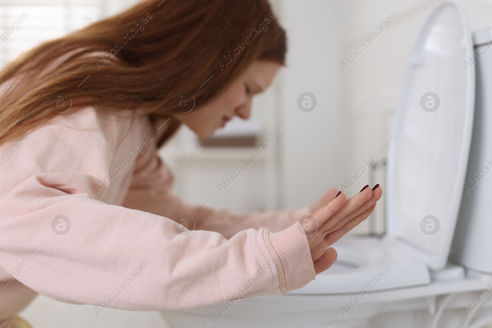 Photo of Teenage girl suffering from nausea over toilet bowl and making stop gesture in bathroom, selective focus. Bulimia