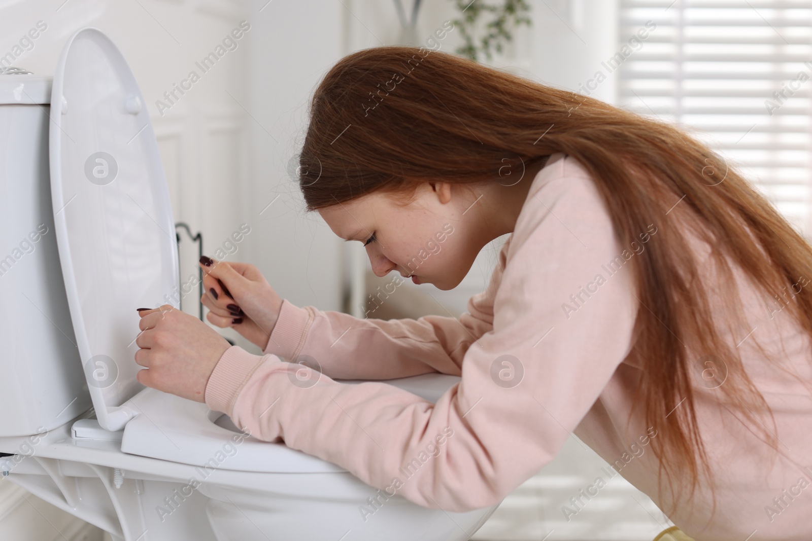 Photo of Teenage girl suffering from nausea over toilet bowl in bathroom. Bulimia