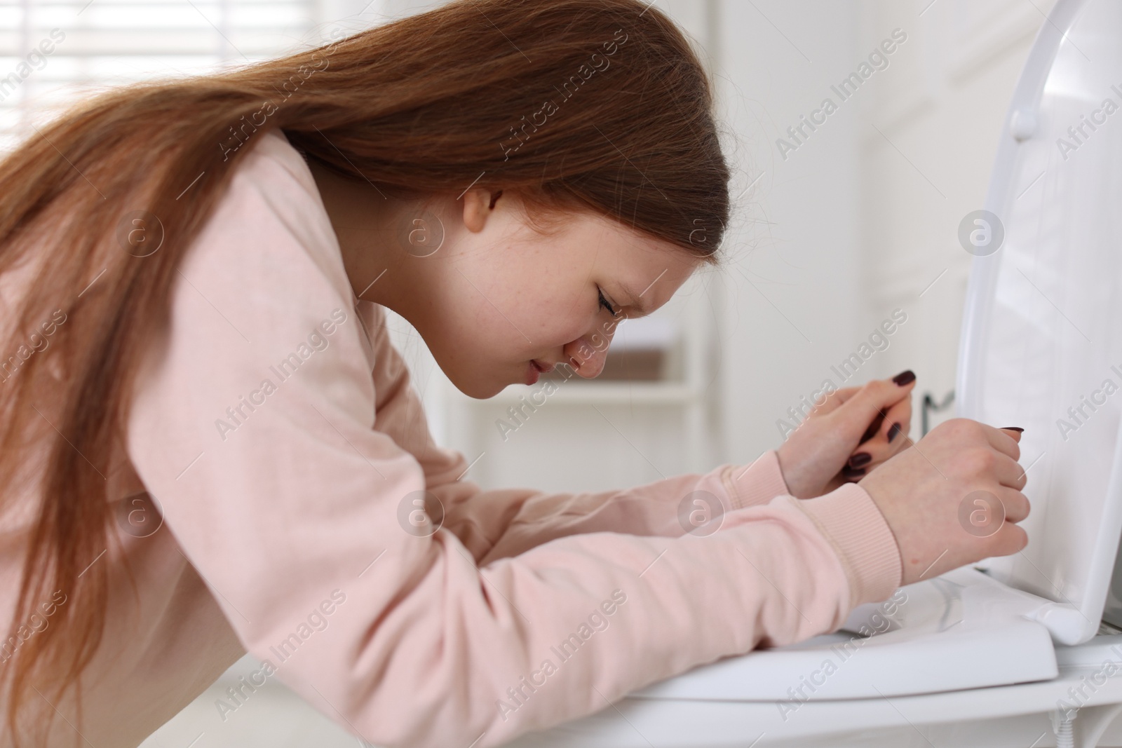 Photo of Teenage girl suffering from nausea over toilet bowl in bathroom. Bulimia