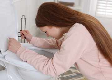 Teenage girl suffering from nausea over toilet bowl in bathroom. Bulimia