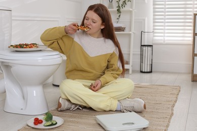 Photo of Teenage girl eating pizza near toilet bowl in bathroom. Bulimia