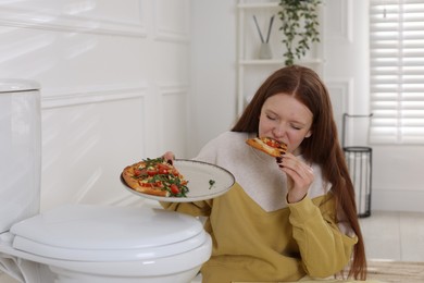 Photo of Teenage girl eating pizza near toilet bowl in bathroom. Bulimia