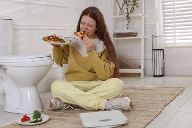 Photo of Teenage girl eating pizza near toilet bowl in bathroom. Bulimia