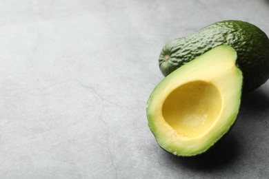 Photo of Whole and cut avocados on light grey table, closeup. Space for text