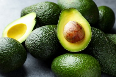 Photo of Many whole and cut avocados on light grey table, closeup