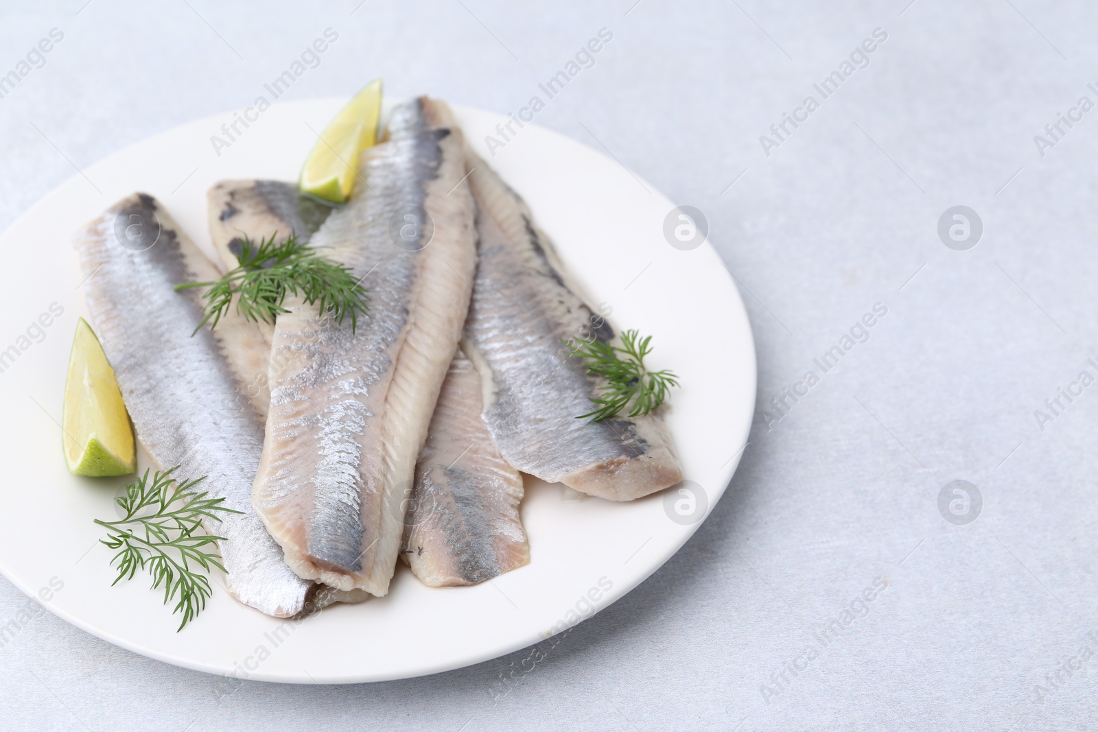 Photo of Marinated herring fillets with lime and dill on grey table, closeup. Space for text