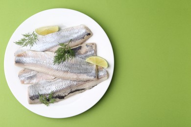 Photo of Marinated herring fillets with lime and dill on green background, top view. Space for text