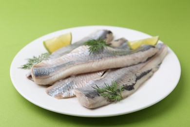 Photo of Marinated herring fillets with lime and dill on green background, closeup