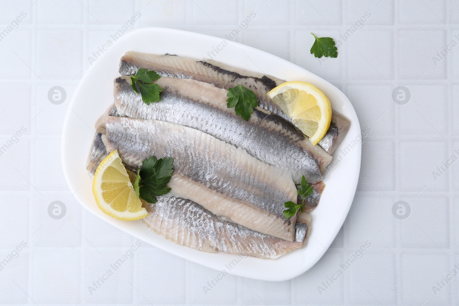 Photo of Marinated herring fillets with lemon and parsley on white tiled table, top view