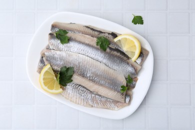 Marinated herring fillets with lemon and parsley on white tiled table, top view