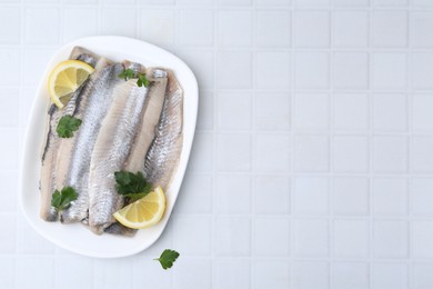 Marinated herring fillets with lemon and parsley on white tiled table, top view. Space for text