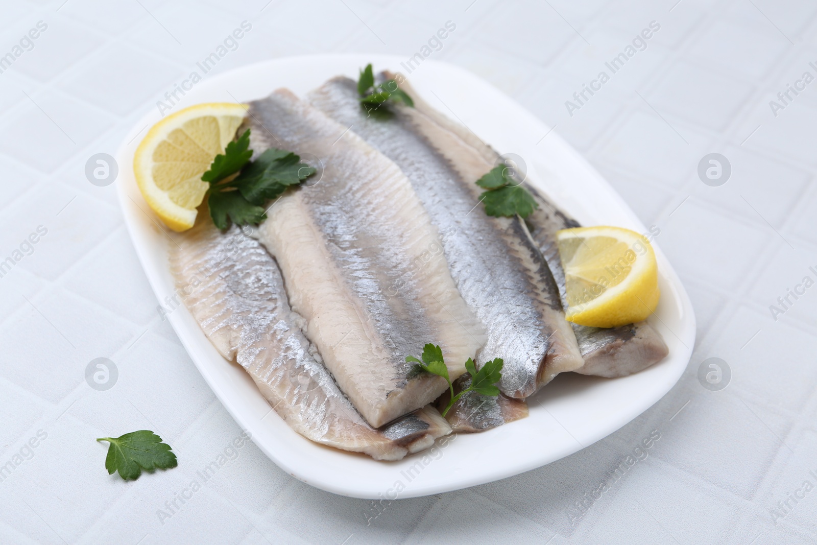 Photo of Marinated herring fillets with lemon and parsley on white tiled table, closeup