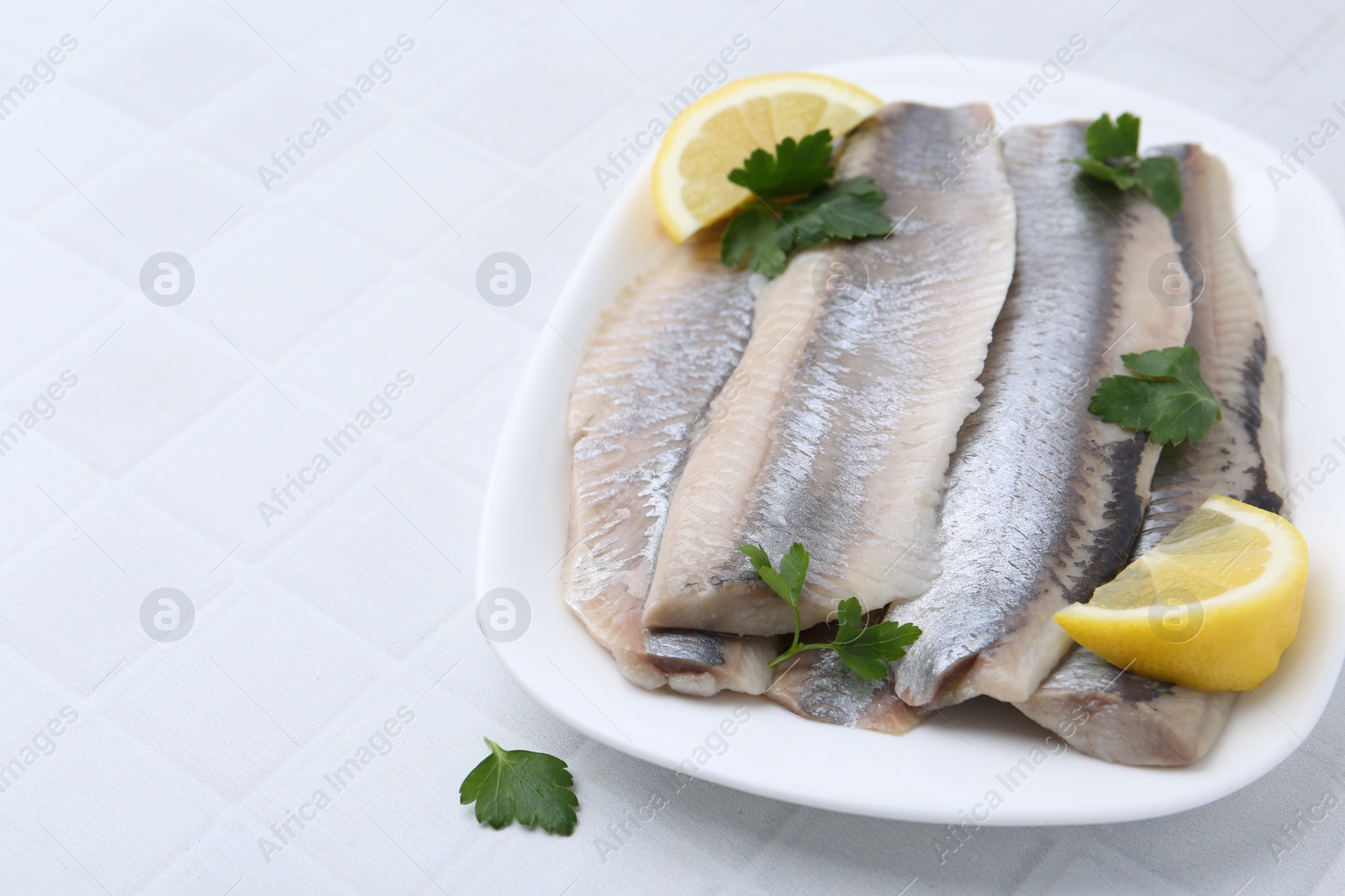 Photo of Marinated herring fillets with lemon and parsley on white tiled table, closeup. Space for text