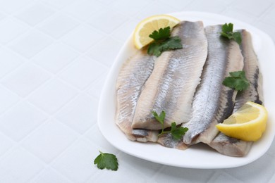 Marinated herring fillets with lemon and parsley on white tiled table, closeup. Space for text