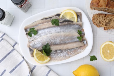 Photo of Marinated herring fillets with lemon, parsley and spices on white tiled table, flat lay