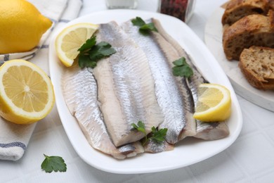 Marinated herring fillets with lemon and parsley on white tiled table, closeup