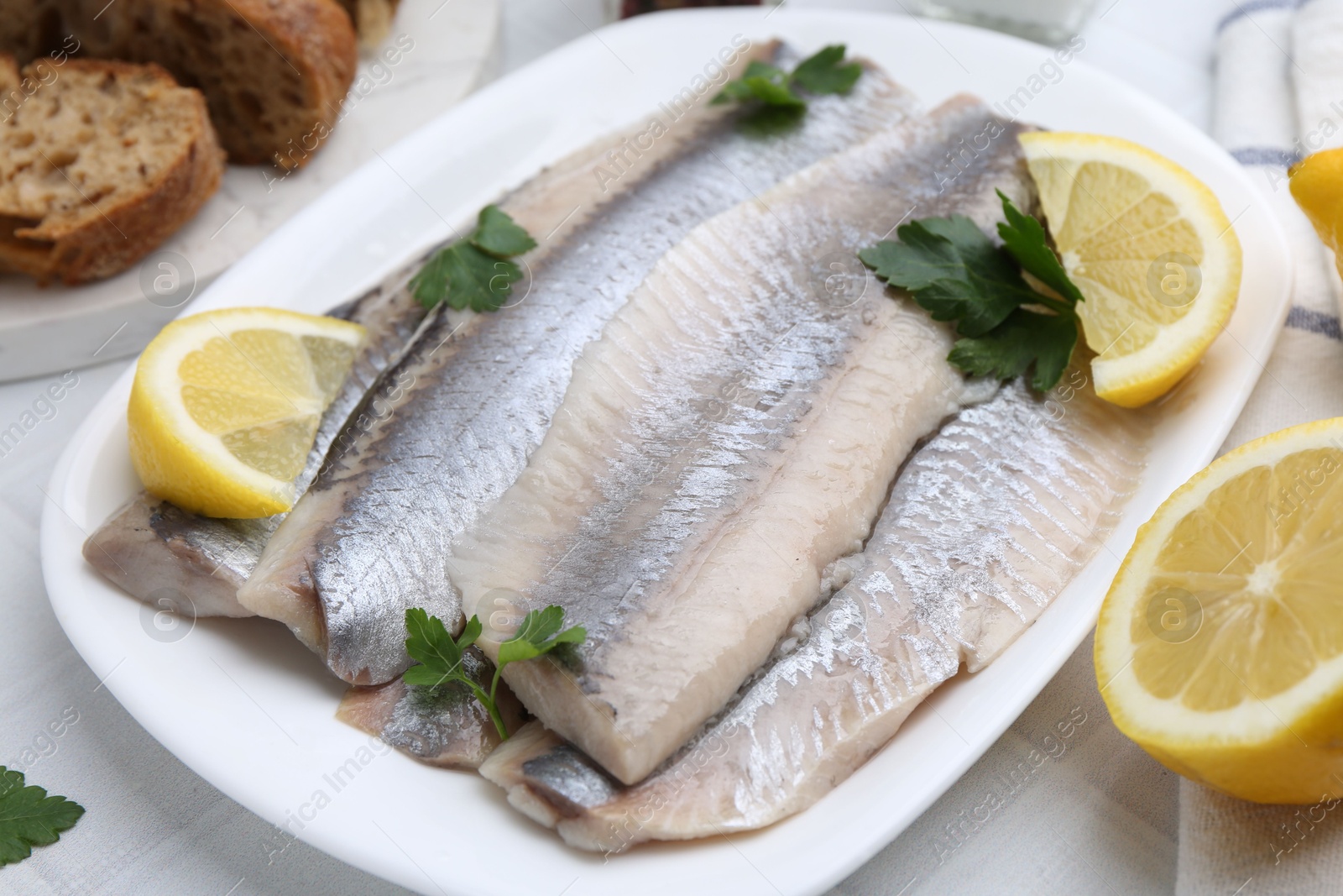 Photo of Marinated herring fillets with lemon and parsley on white tiled table, closeup