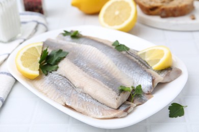 Marinated herring fillets with lemon and parsley on white tiled table, closeup