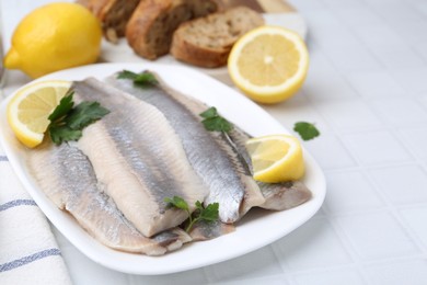 Marinated herring fillets with lemon and parsley on white tiled table, closeup