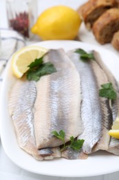 Photo of Marinated herring fillets with lemon and parsley on white table, closeup