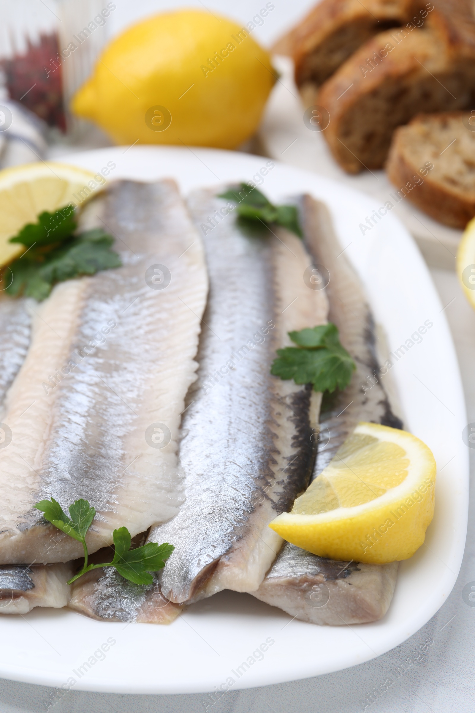 Photo of Marinated herring fillets with lemon and parsley on white table, closeup