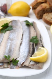 Marinated herring fillets with lemon and parsley on white table, closeup