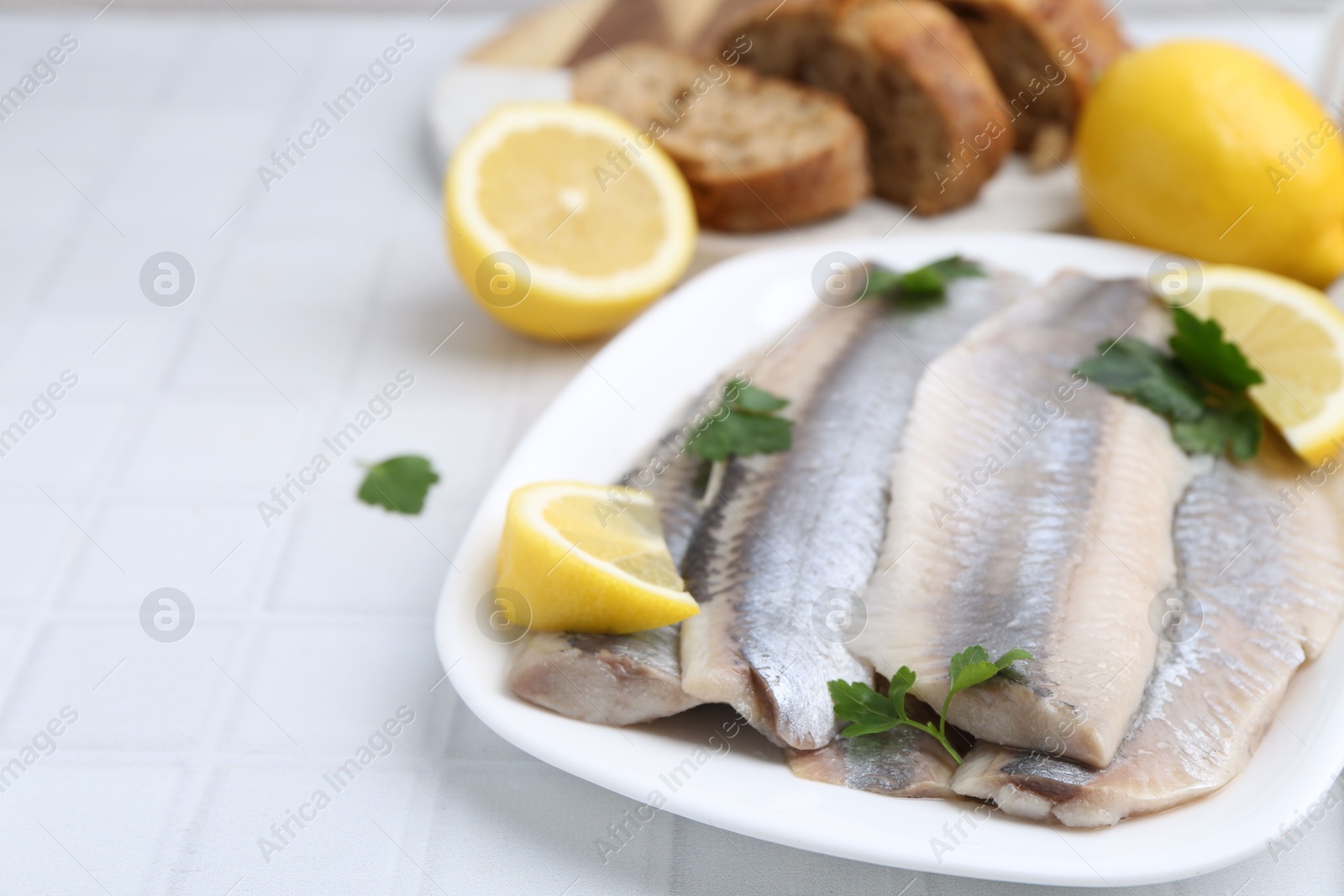 Photo of Marinated herring fillets with lemon and parsley on white tiled table, closeup. Space for text