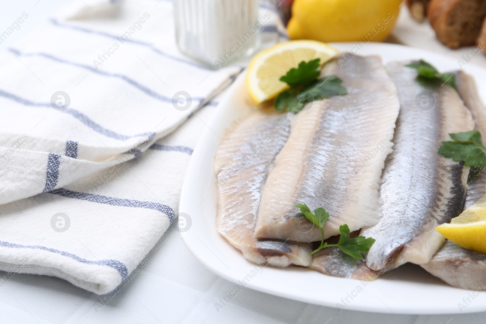 Photo of Marinated herring fillets with lemon and parsley on white tiled table, closeup