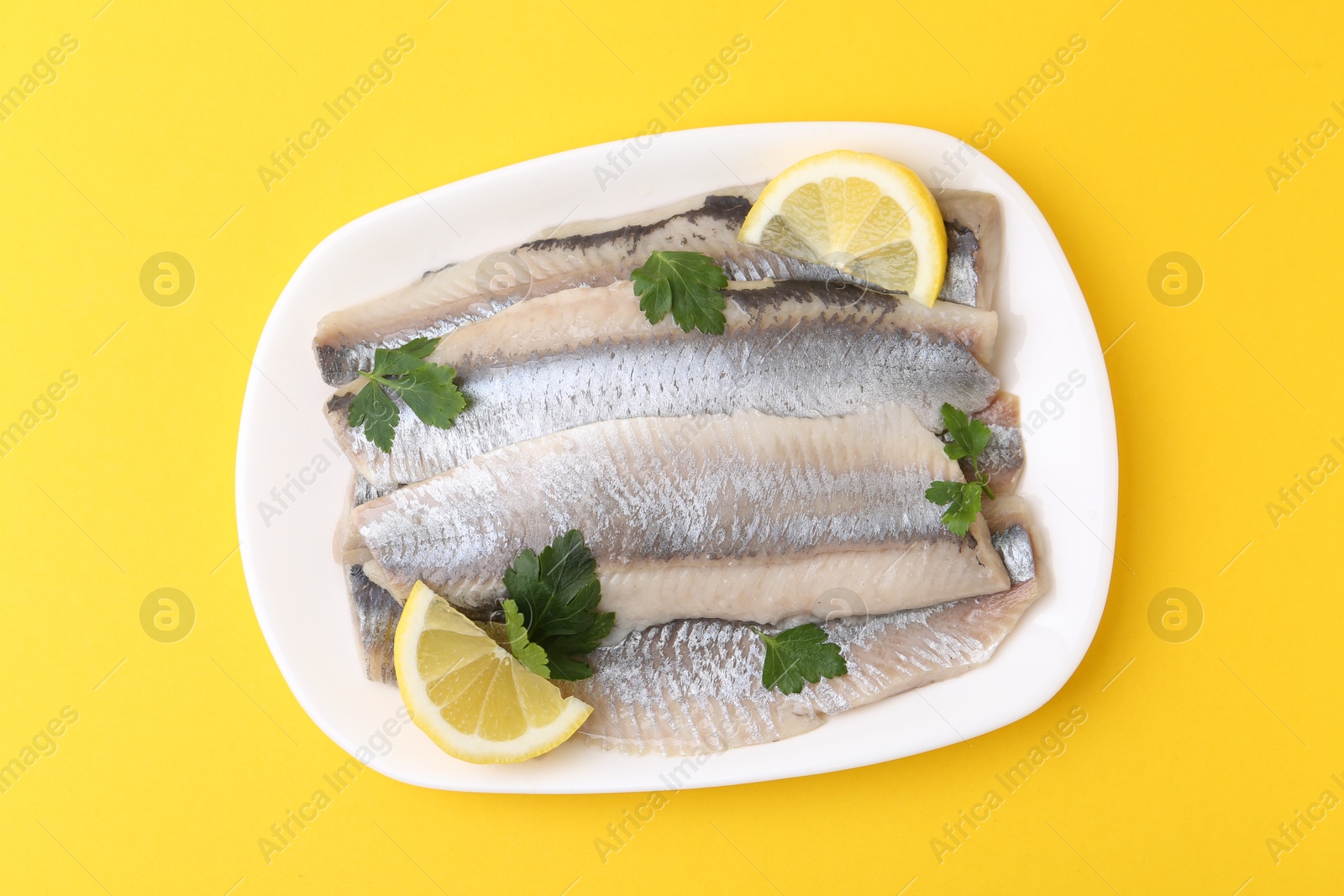 Photo of Marinated herring fillets with lemon and parsley on yellow background, top view