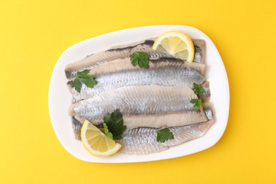 Marinated herring fillets with lemon and parsley on yellow background, top view