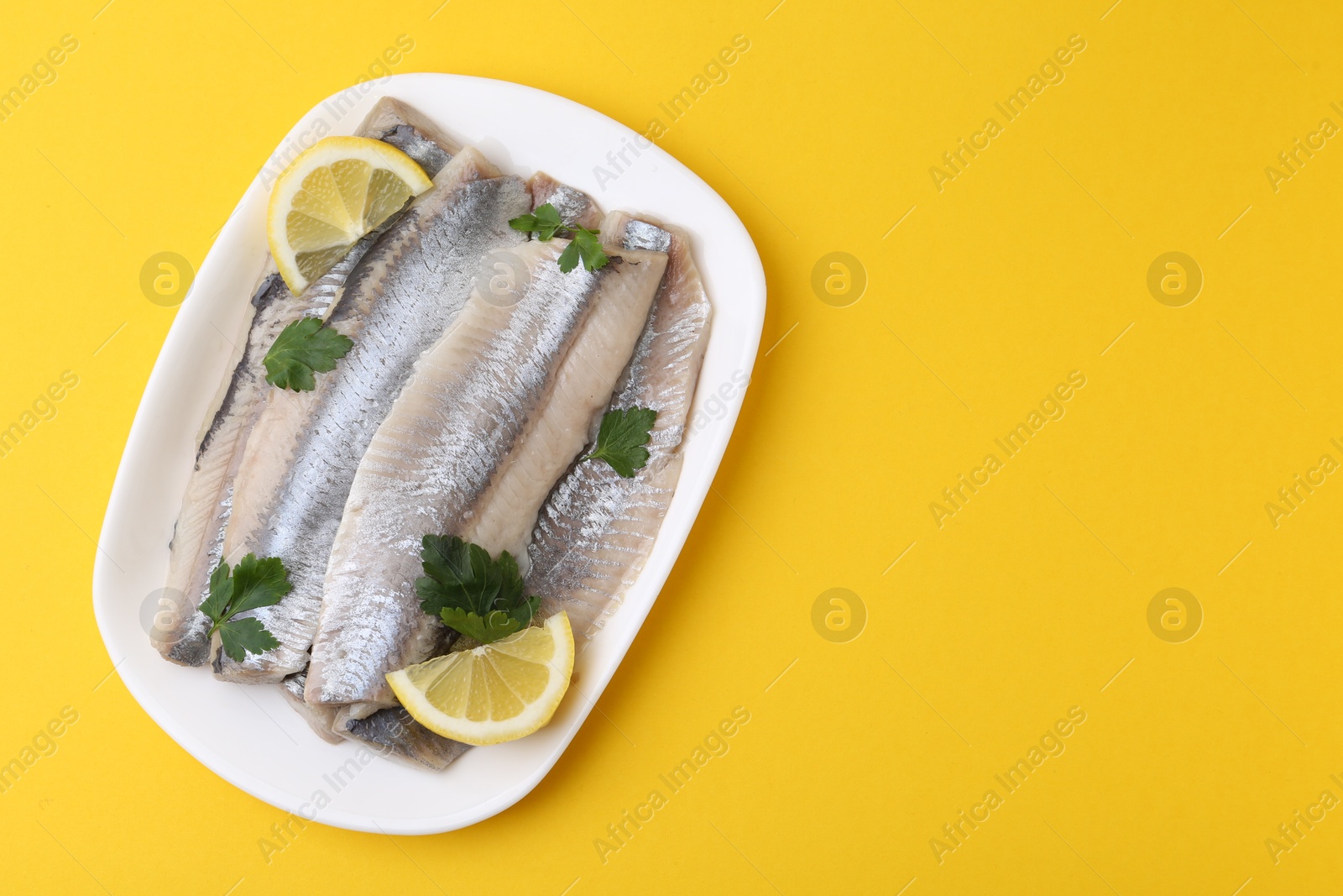 Photo of Marinated herring fillets with lemon and parsley on yellow background, top view. Space for text