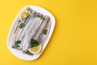 Marinated herring fillets with lemon and parsley on yellow background, top view. Space for text