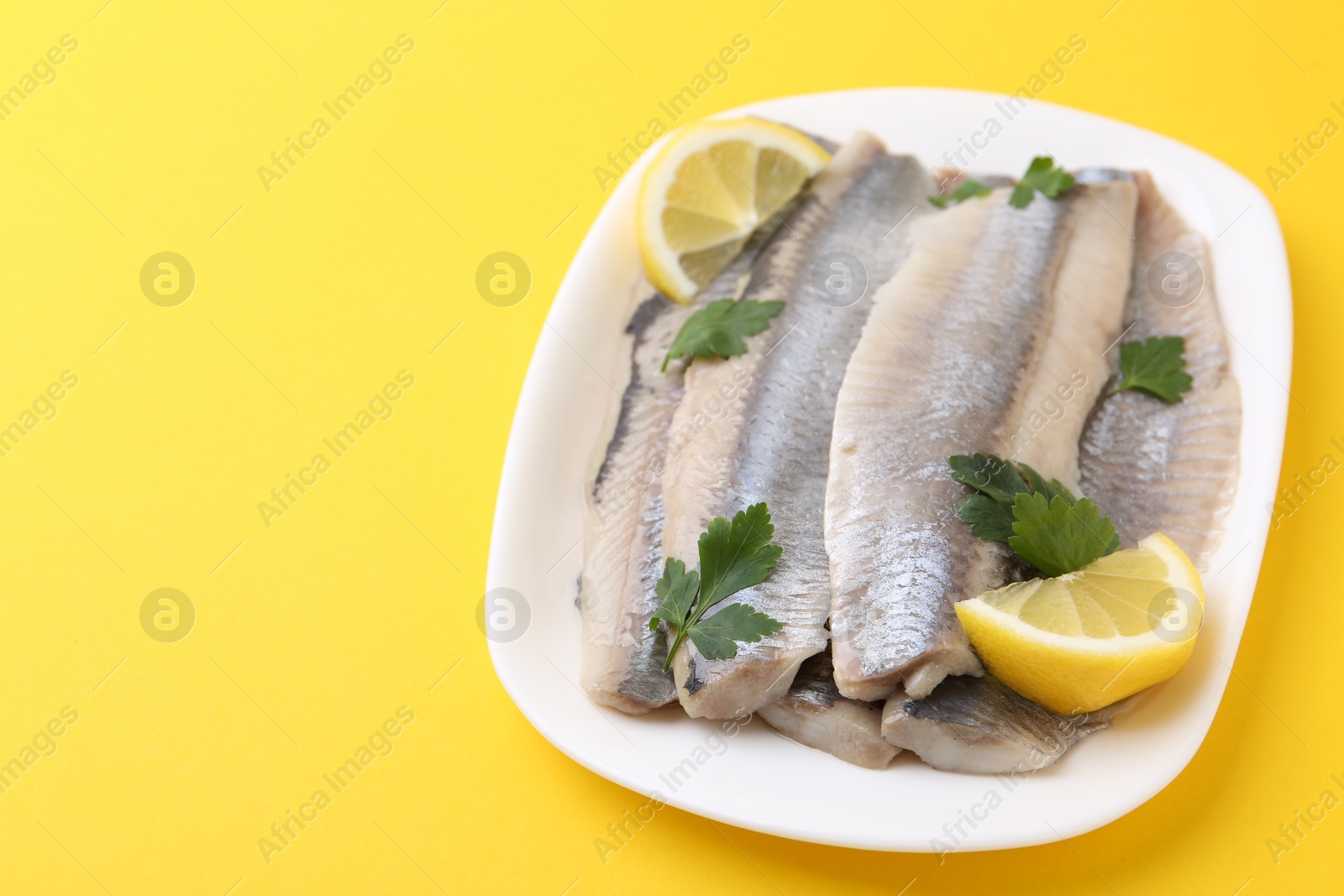 Photo of Marinated herring fillets with lemon and parsley on yellow background, closeup. Space for text