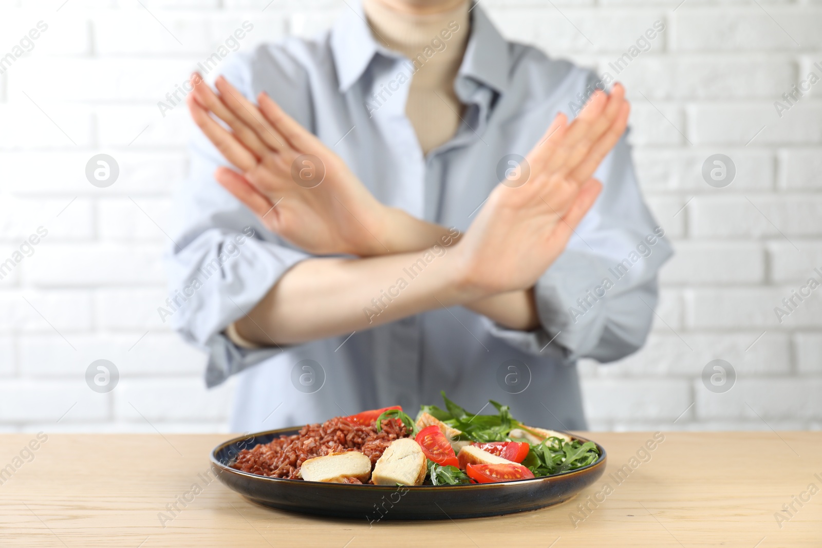 Photo of Woman refusing to eat meal at wooden table near white brick wall, selective focus. Food allergy concept