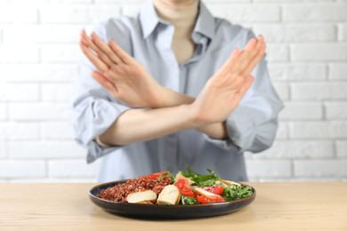 Photo of Woman refusing to eat meal at wooden table near white brick wall, selective focus. Food allergy concept