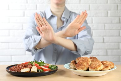 Photo of Woman refusing to eat products at wooden table near white brick wall, selective focus. Food allergy concept