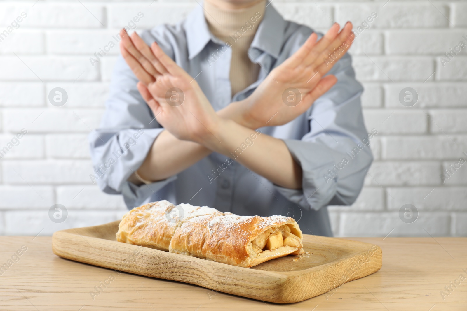 Photo of Woman refusing to eat apple strudel at wooden table near white brick wall, selective focus. Food allergy concept