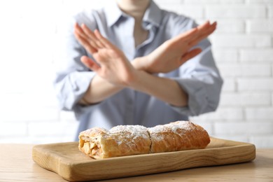 Photo of Woman refusing to eat apple strudel at wooden table near white brick wall, selective focus. Food allergy concept