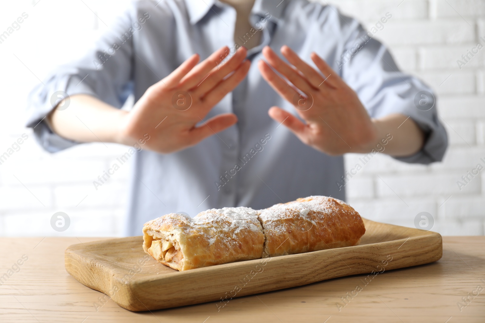 Photo of Woman refusing to eat apple strudel at wooden table near white brick wall, selective focus. Food allergy concept