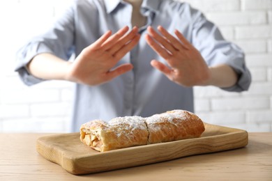 Photo of Woman refusing to eat apple strudel at wooden table near white brick wall, selective focus. Food allergy concept