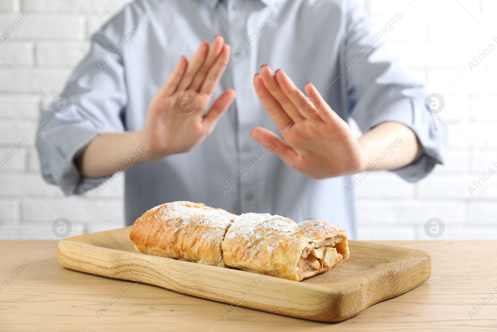 Photo of Woman refusing to eat apple strudel at wooden table near white brick wall, selective focus. Food allergy concept