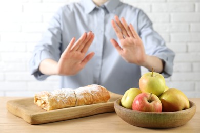 Photo of Woman refusing to eat products at wooden table near white brick wall, selective focus. Food allergy concept