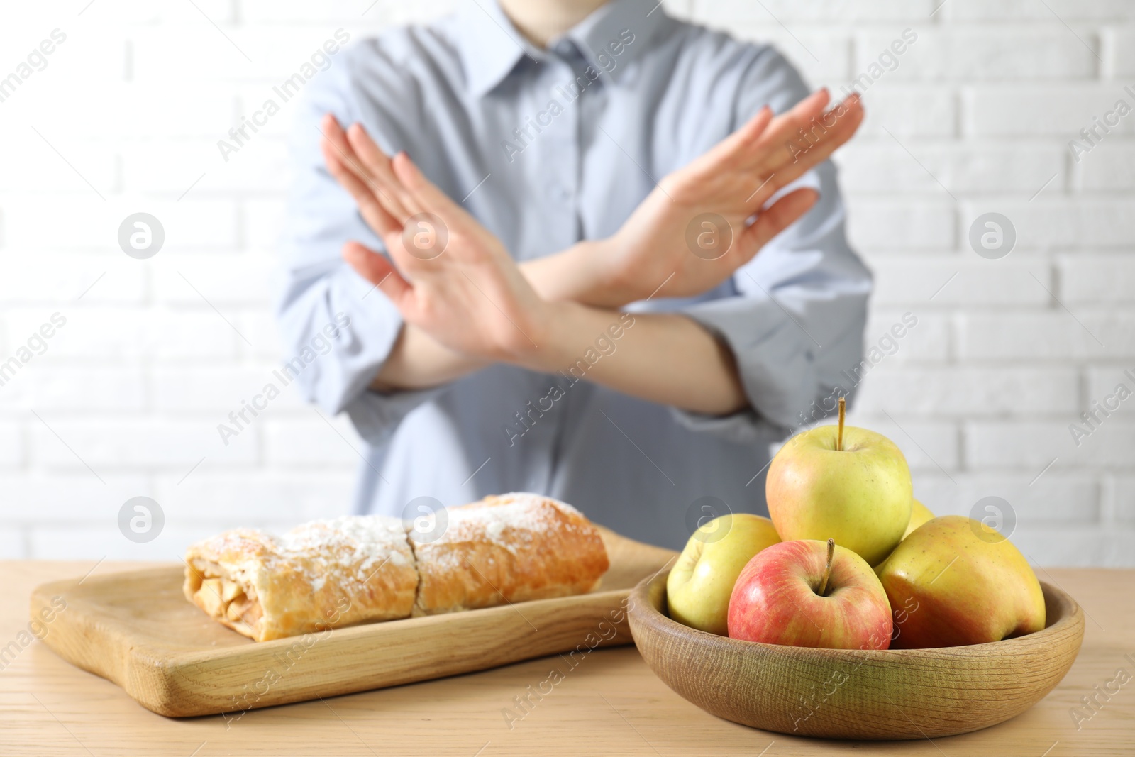 Photo of Woman refusing to eat products at wooden table near white brick wall, selective focus. Food allergy concept