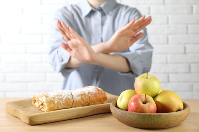 Photo of Woman refusing to eat products at wooden table near white brick wall, selective focus. Food allergy concept