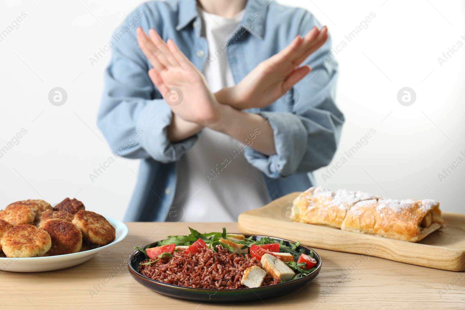 Photo of Woman refusing to eat products at wooden table near white brick wall, selective focus. Food allergy concept