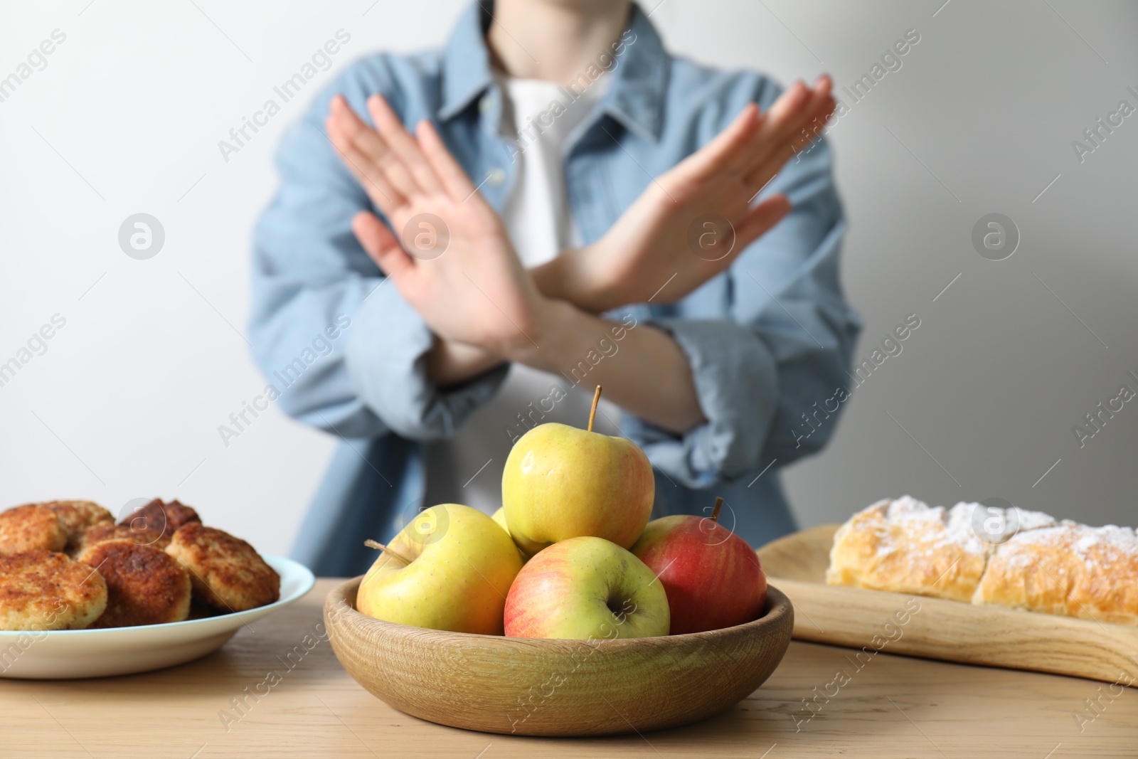 Photo of Woman refusing to eat products at wooden table near white brick wall, selective focus. Food allergy concept