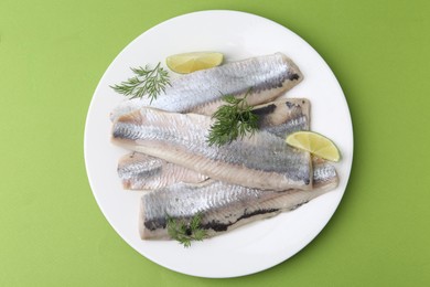 Photo of Marinated herring fillets with lime and dill on green background, top view