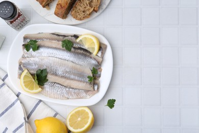 Marinated herring fillets with lemon, parsley and spices on white tiled table, flat lay. Space for text